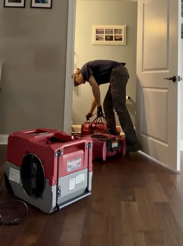 Restoration tech setting a dehumidifier on a wet hardwood floor in an Escondido home
