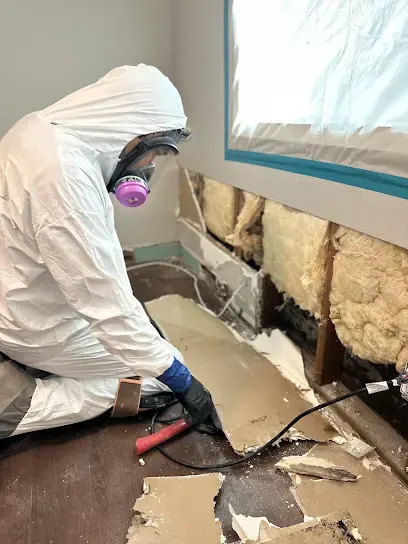 Tech in a protective suit and respirator removing wet drywall after a sewage backup in Escondido